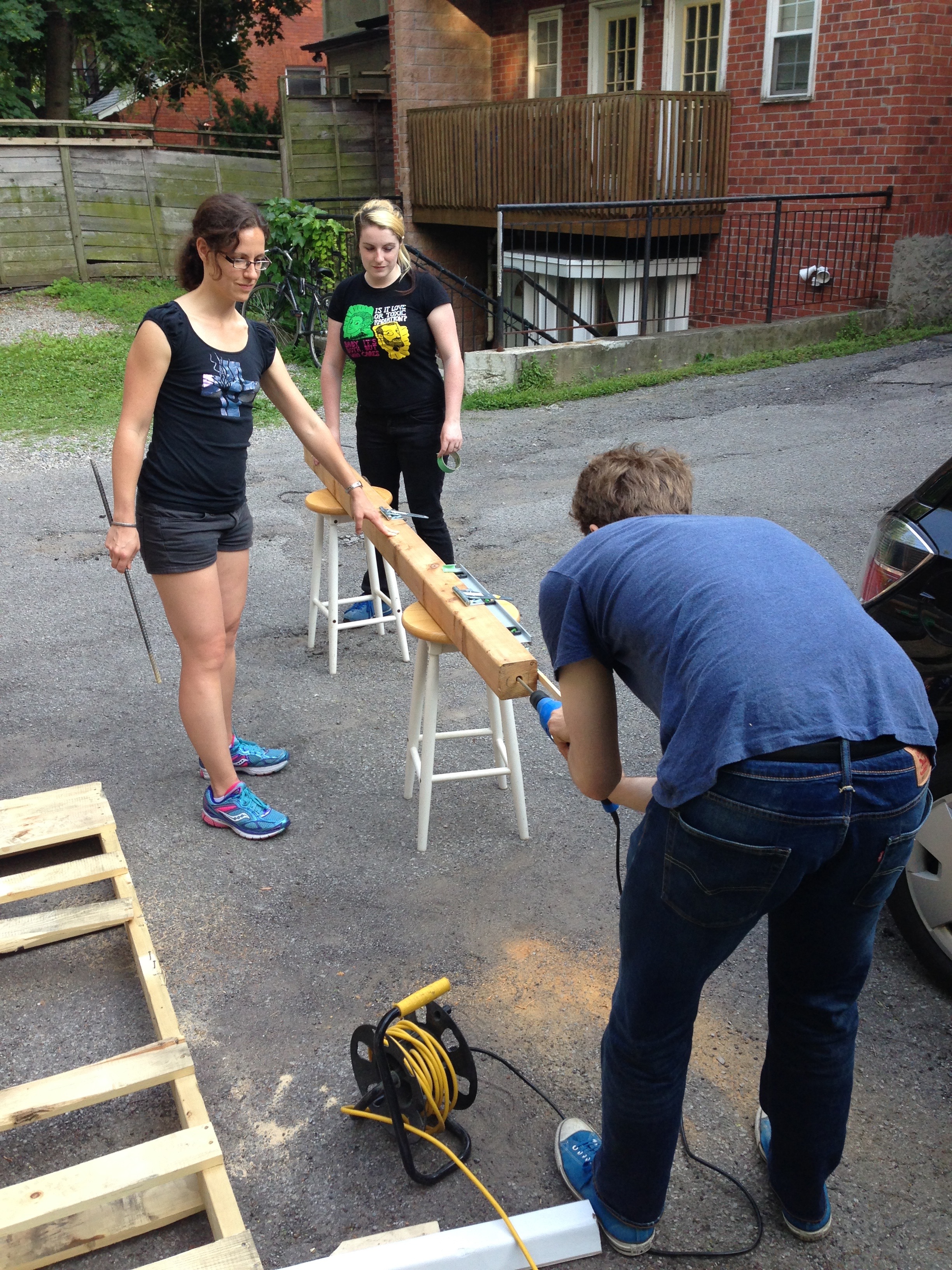 Mel and Geoff help S drill a post.